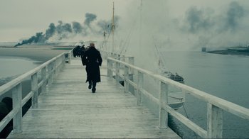 Movie still from “Dunkirk” (2017), directed by Christopher Nolan – A person walking on a pier with smoke billowing out of it; Extreme Wide shot, High angle