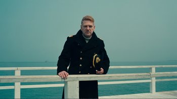 Movie still from “Dunkirk” (2017), directed by Christopher Nolan – A man in a military uniform standing on a pier; Medium shot, Low angle