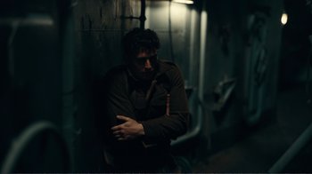 Movie still from “Dunkirk” (2017), directed by Christopher Nolan – A man standing in the dark with his arms crossed; Medium shot, Over the shoulder angle