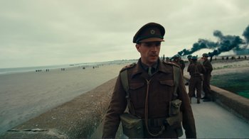 Movie still from “Dunkirk” (2017), directed by Christopher Nolan – A man in a military uniform walking on the beach; Medium shot, Low angle