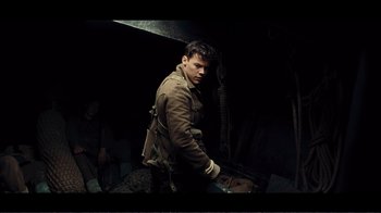 Movie still from “Dunkirk” (2017), directed by Christopher Nolan – A young man in a trench coat and a backpack; Medium shot, High angle