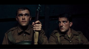 Movie still from “Dunkirk” (2017), directed by Christopher Nolan – Two men dressed in military uniforms holding a rifle; Medium shot, Low angle