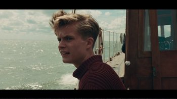 Movie still from “Dunkirk” (2017), directed by Christopher Nolan – A young man standing on top of a boat in the water; Close Up shot, Over the shoulder angle