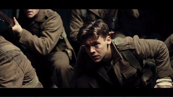 Movie still from “Dunkirk” (2017), directed by Christopher Nolan – A young man in a military uniform sitting on the ground; Medium shot, High angle