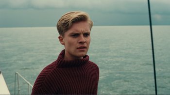 Movie still from “Dunkirk” (2017), directed by Christopher Nolan – A young man in a red sweater is standing in front of the ocean; Close Up shot, Over the shoulder angle