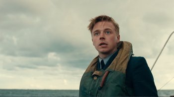 Movie still from “Dunkirk” (2017), directed by Christopher Nolan – A young man in a green jacket looks into the distance; Close Up shot, Low angle