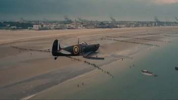 Movie still from “Dunkirk” (2017), directed by Christopher Nolan – An airplane is flying over the water on the beach; Extreme Wide shot, High angle