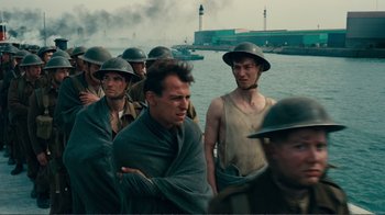 Movie still from “Dunkirk” (2017), directed by Christopher Nolan – A group of men in military uniforms standing next to a body of water; Medium shot, Low angle