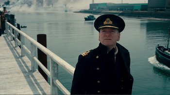 Movie still from “Dunkirk” (2017), directed by Christopher Nolan – A man in a uniform standing on a pier; Medium shot, Low angle