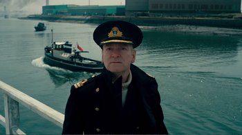 Movie still from “Dunkirk” (2017), directed by Christopher Nolan – A man in a military uniform standing in front of a body of water; Medium shot, Low angle