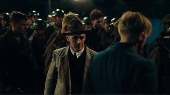Movie still from “Dunkirk” (2017), directed by Christopher Nolan – An old man in a suit and a hat talking to a crowd of people; Medium shot, Over the shoulder angle