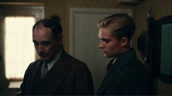 Movie still from “Dunkirk” (2017), directed by Christopher Nolan – Two men in suits standing next to each other in a room; Medium shot, Over the shoulder angle