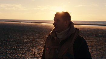 Movie still from “Dunkirk” (2017), directed by Christopher Nolan – A man standing on the beach in front of the sun; Close Up shot, Low angle