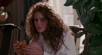 Movie still from “Pretty Woman” (1990), directed by Garry Marshall – A woman sitting in a chair holding a sandwich; Close Up shot, Over the shoulder angle