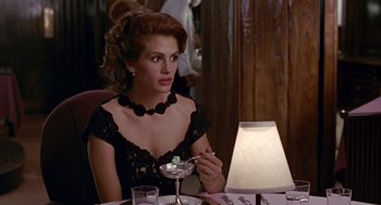 Movie still from “Pretty Woman” (1990), directed by Garry Marshall – A woman sitting at a table with a glass of wine; Medium shot, Over the shoulder angle