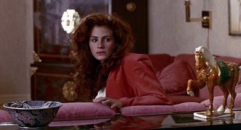Movie still from “Pretty Woman” (1990), directed by Garry Marshall – A woman sitting on top of a pink couch in a living room; Medium shot, Over the shoulder angle