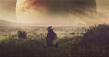 A person sitting in a field near a wire fence