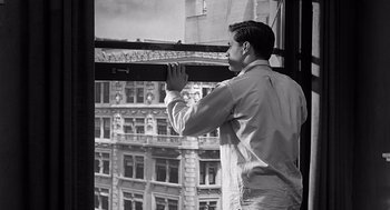 Movie still from “Psycho” (1960), directed by Alfred Hitchcock – A black and white photo of a man looking out of a window; Medium shot, Low angle