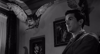Movie still from “Psycho” (1960), directed by Alfred Hitchcock – A black and white photo of a man in a room with an owl; Close Up shot, Low angle
