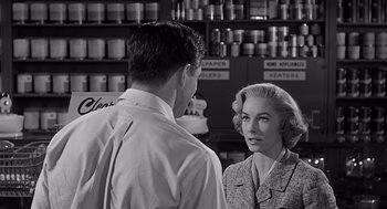 Movie still from “Psycho” (1960), directed by Alfred Hitchcock – A man and a woman are standing in front of a counter; Medium shot, Over the shoulder angle