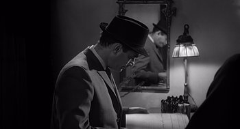 Movie still from “Psycho” (1960), directed by Alfred Hitchcock – A black and white photo of a man in a suit and hat; Close Up shot, High angle