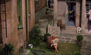 Movie still from “Rear Window” (1954), directed by Alfred Hitchcock – A woman sitting in a lawn chair reading a book; Wide shot, High angle