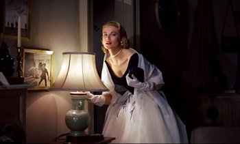 Movie still from “Rear Window” (1954), directed by Alfred Hitchcock – A beautiful woman in a white dress holding a lamp next to a table; Medium shot, Low angle