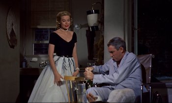 Movie still from “Rear Window” (1954), directed by Alfred Hitchcock – A man and a woman are sitting in front of a wine glass; Medium shot, Low angle