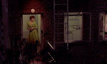 Movie still from “Rear Window” (1954), directed by Alfred Hitchcock – A woman in a green dress standing in a door way; Wide shot, Low angle