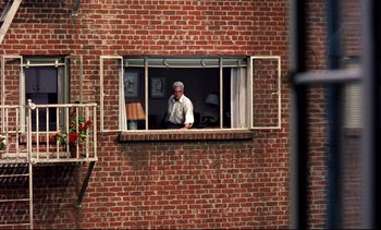 Movie still from “Rear Window” (1954), directed by Alfred Hitchcock – A man standing in the window of a brick building; Wide shot, Low angle