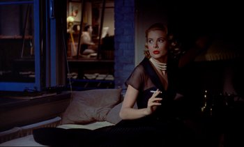 Movie still from “Rear Window” (1954), directed by Alfred Hitchcock – A woman sitting on a couch holding a cigarette in her hand; Medium shot, Over the shoulder angle