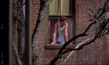 Movie still from “Rear Window” (1954), directed by Alfred Hitchcock – A man leaning up against a brick building window; Medium shot, Low angle