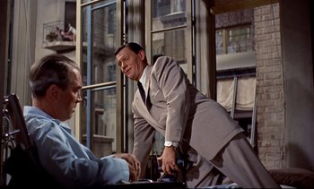 Movie still from “Rear Window” (1954), directed by Alfred Hitchcock – A man standing next to another man in front of a window; Medium shot, Over the shoulder angle