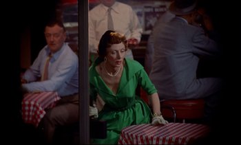 Movie still from “Rear Window” (1954), directed by Alfred Hitchcock – A woman in a green dress sitting at a table; Medium shot, Over the shoulder angle