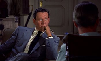 Movie still from “Rear Window” (1954), directed by Alfred Hitchcock – A man in a suit and tie sitting in front of another man; Close Up shot, Over the shoulder angle