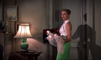 Movie still from “Rear Window” (1954), directed by Alfred Hitchcock – A woman in a white shirt and green pants holding a bag; Medium shot, Low angle