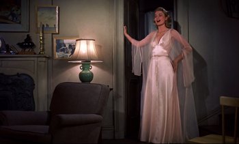 Movie still from “Rear Window” (1954), directed by Alfred Hitchcock – A woman standing in a living room wearing a white dress; Medium shot, Low angle