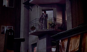 Movie still from “Rear Window” (1954), directed by Alfred Hitchcock – Two people are standing on a balcony looking out the window; Wide shot, Low angle
