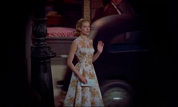 Movie still from “Rear Window” (1954), directed by Alfred Hitchcock – A woman wearing a dress and holding her hand out to someone; Medium shot, Low angle
