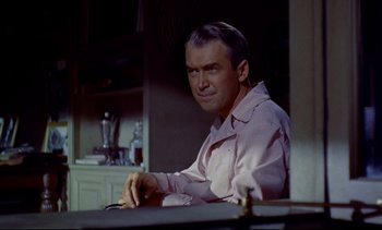 Movie still from “Rear Window” (1954), directed by Alfred Hitchcock – A man sitting at a table in front of a bottle; Medium shot, Over the shoulder angle