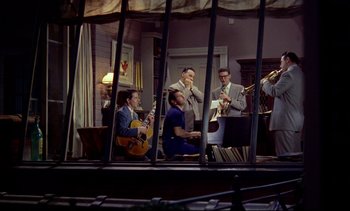 Movie still from “Rear Window” (1954), directed by Alfred Hitchcock – A group of men sitting in a living room playing instruments; Wide shot, High angle