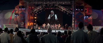 Movie still from “Richard Jewell” (2019), directed by Clint Eastwood – A crowd of people standing on a stage with musical instruments; Wide shot, Over the shoulder angle