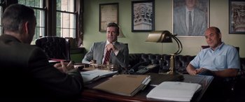Movie still from “Richard Jewell” (2019), directed by Clint Eastwood – A man sitting at a desk in front of papers and a lamp; Medium shot, Over the shoulder angle