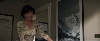 Movie still from “Richard Jewell” (2019), directed by Clint Eastwood – A woman standing in front of a picture of a snowy mountain; Medium shot, Low angle