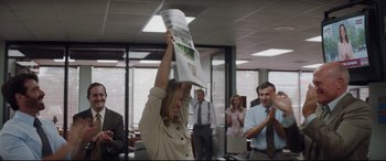 Movie still from “Richard Jewell” (2019), directed by Clint Eastwood – A woman holding up a newspaper above her head in an office setting; Medium shot, Low angle