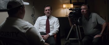 Movie still from “Richard Jewell” (2019), directed by Clint Eastwood – A man sitting in a chair in front of a video camera; Medium shot, Over the shoulder angle