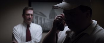 Movie still from “Richard Jewell” (2019), directed by Clint Eastwood – A man talking on a phone while another man sits in the background; Close Up shot, Over the shoulder angle