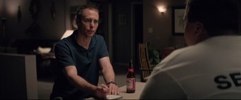 Movie still from “Richard Jewell” (2019), directed by Clint Eastwood – A man sitting at a table with a bottle of beer in front of him; Medium shot, Over the shoulder angle