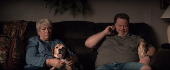 Movie still from “Richard Jewell” (2019), directed by Clint Eastwood – A man and a woman sitting on a couch talking on a phone; Medium shot, High angle