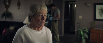 Movie still from “Richard Jewell” (2019), directed by Clint Eastwood – An older woman in a white t - shirt is in a dark room; Close Up shot, Over the shoulder angle